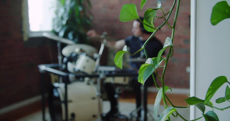 A man wearing headphones plays the drums in an apartment