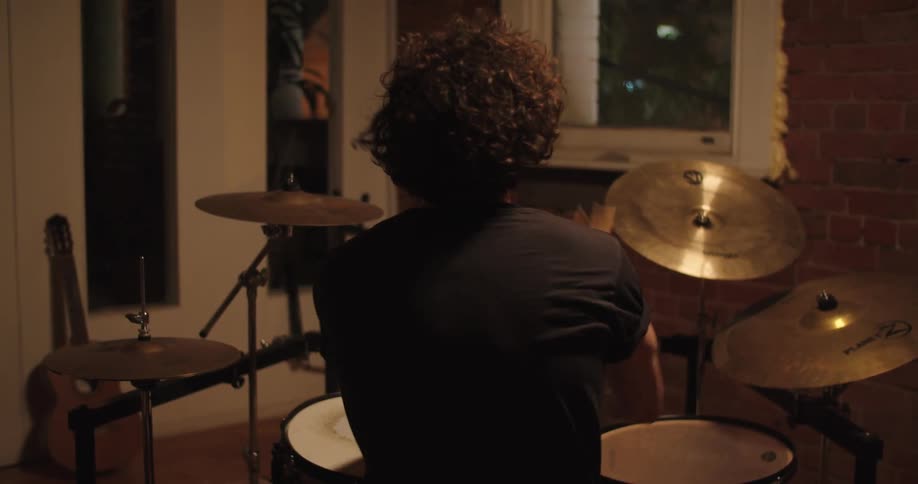 A man drumming on a drum set in a room during the night