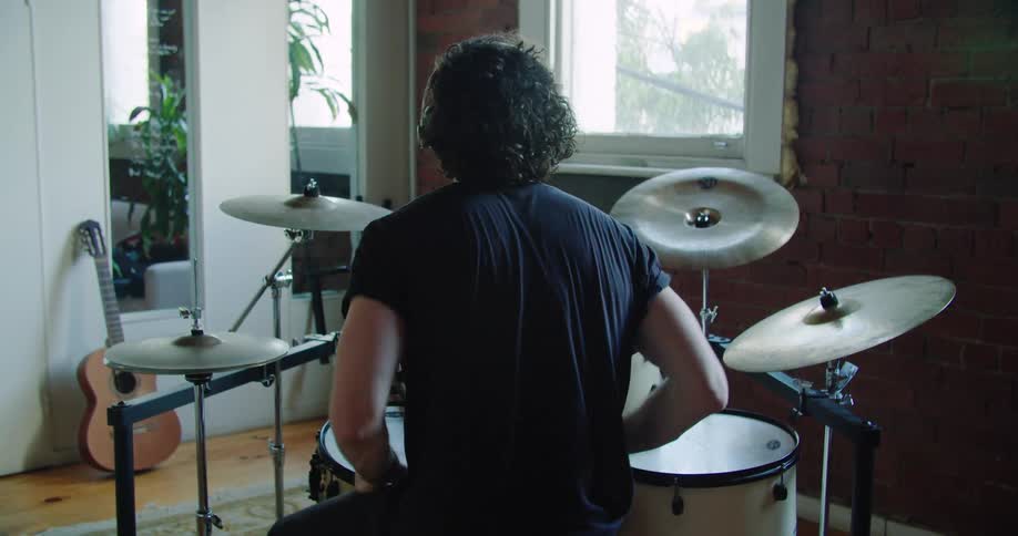 A man drums on a drum set then stands up and takes off his headphones