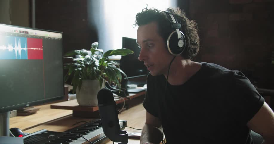 Man sits in front of computer speaking into recording equipment