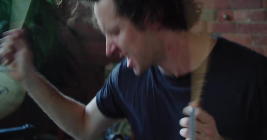 A man drumming energetically indoors during the day
