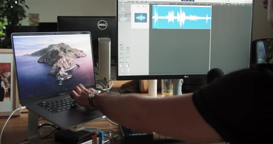A man wears headphones as he uses a laptop and microphone to record audio for film footage