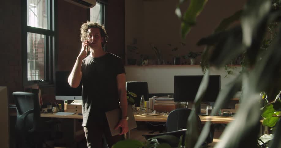 Man standing in front of the desk answers the mobile phone in the office