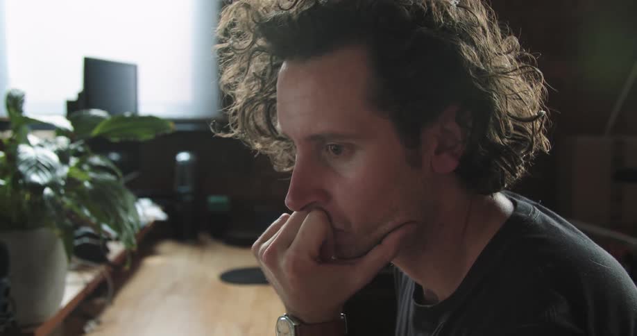 A man leaning his head on his hand nods along to music as he looks from one screen to another