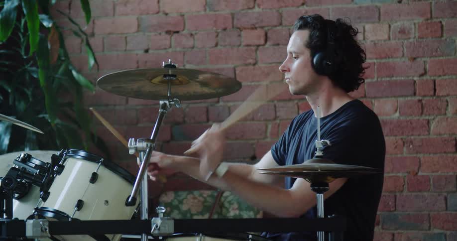 Man wearing headphones plays drums indoors
