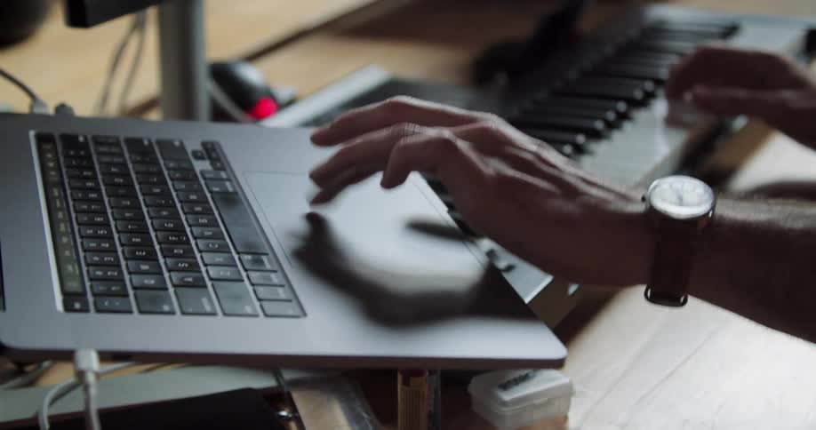 Man plays on a musical keyboard and types and scrolls on a laptop