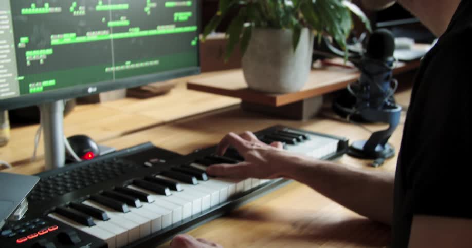 A man nods along as he plays a keyboard and records music on a computer