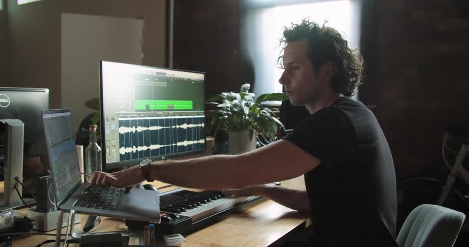 A man nods his head while using a keyboard attached to a laptop and computer monitor