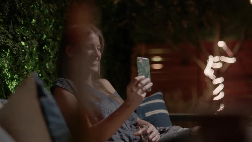 A woman is sitting and using her cell phone to make a video call