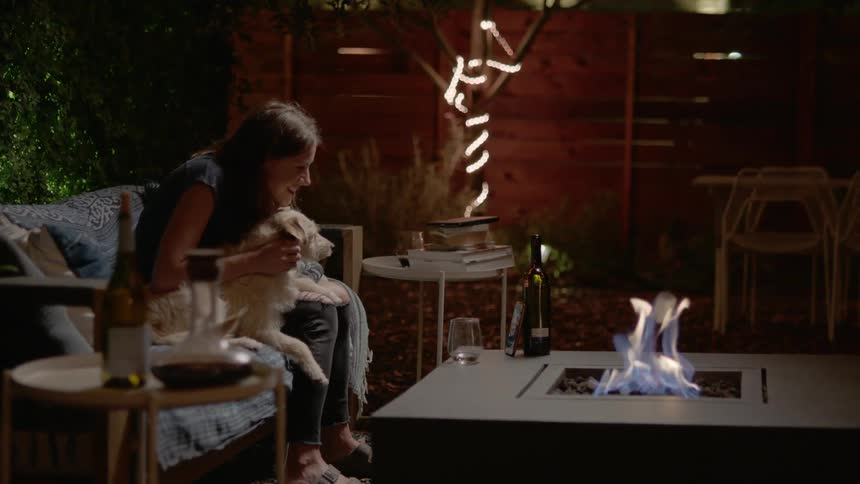 A woman sits by a campfire with a dog