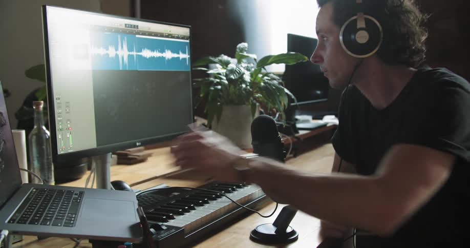 A man with headphones and a microphone sitting at a computer recording his voice