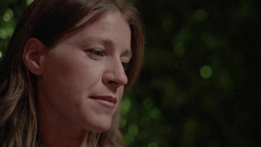 A woman talks to someone off screen at night