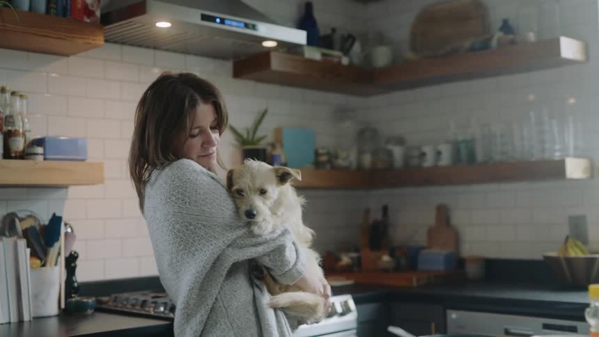 A woman in the kitchen holding a dog