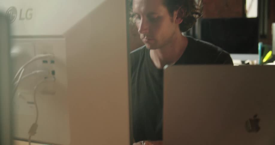 A man with crazy curly hair plays a keyboard in front of a computer monitor