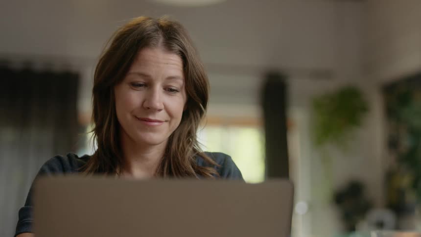 A woman smiles and tilts her head to the side as she closes her laptop
