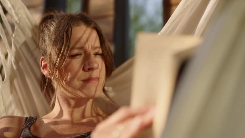 A woman reading a book while resting in a hammock
