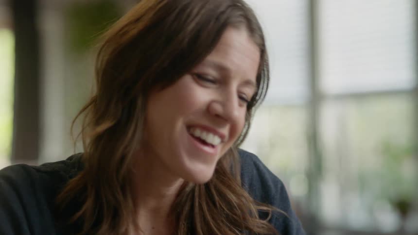 Woman sits laughing in brightly lit room
