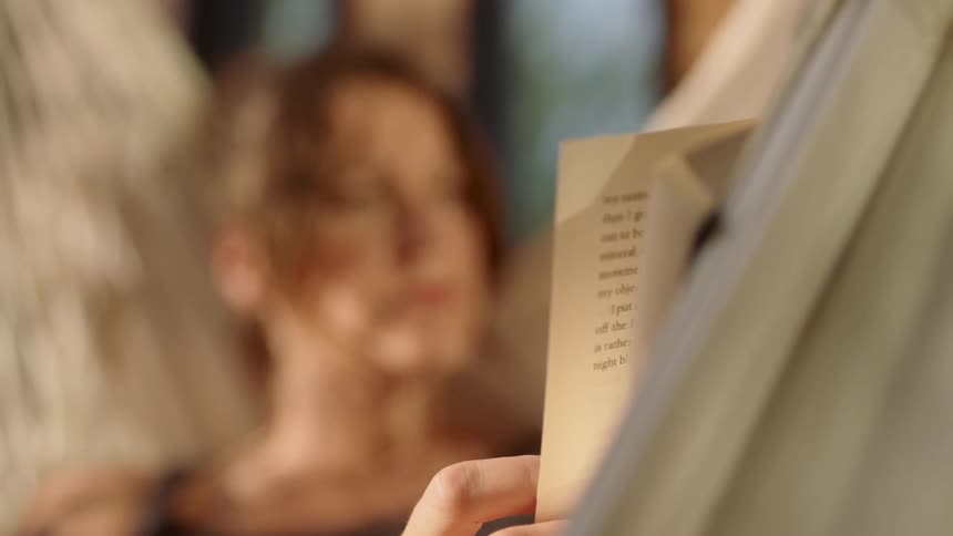 A woman reads a book while sitting in a hammock
