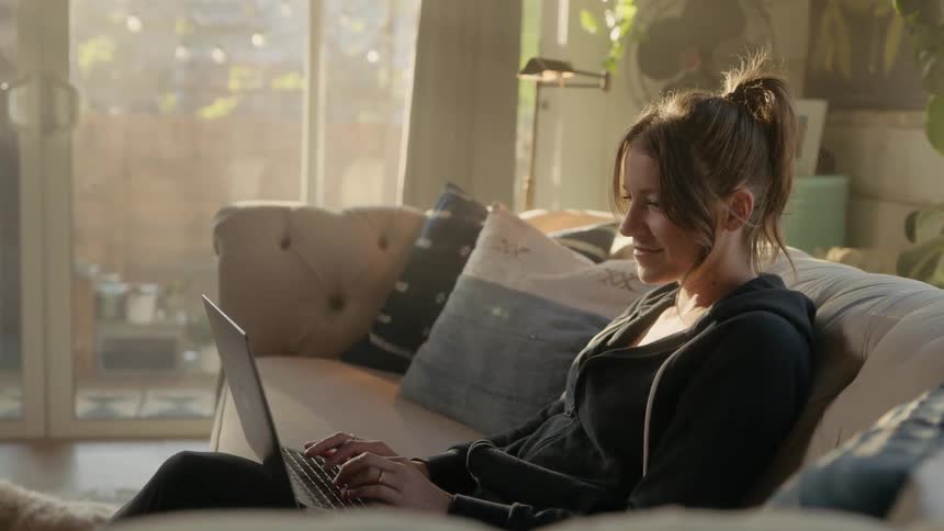 A woman smiling while typing on a laptop in a living room