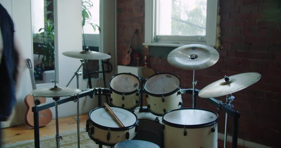 A man sitting behind a drum set rests his sticks on the snare drum stands up and walks away