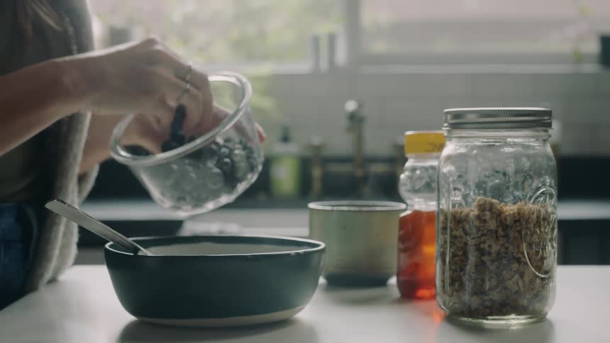 A person dropping berries in a bowl while standing in a kitchen