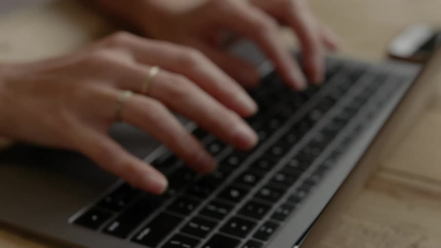 A person sitting at a table typing on a laptop
