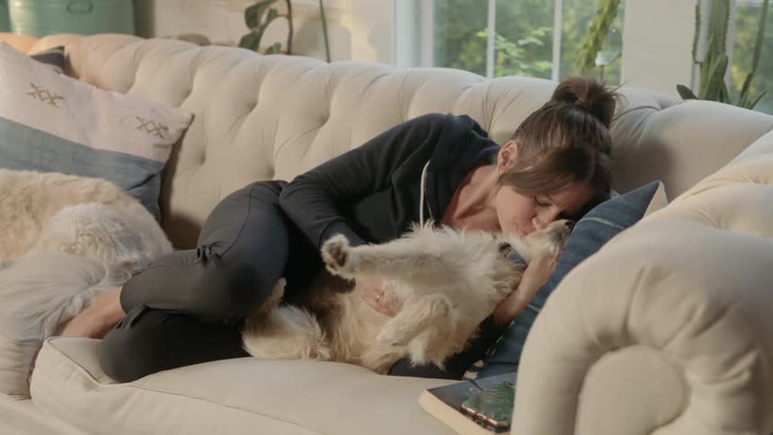 A woman cuddling and petting a dog while laying on a sofa