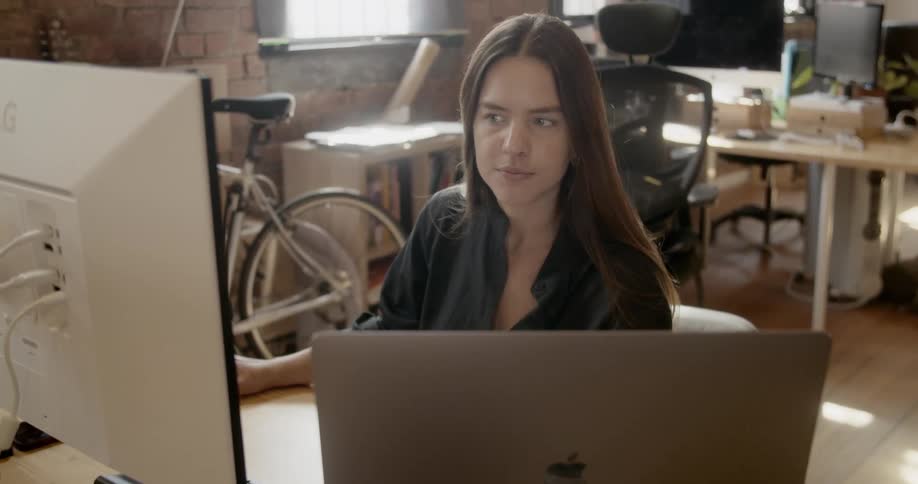 A woman works on a laptop and desktop computer