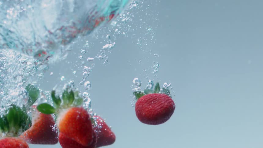 Strawberries fall through water creating bubbles
