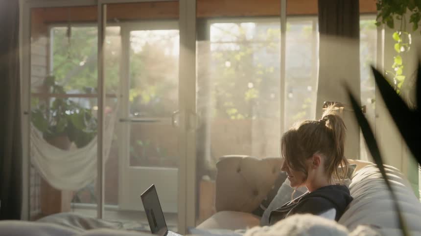 A woman sits on the couch using her laptop