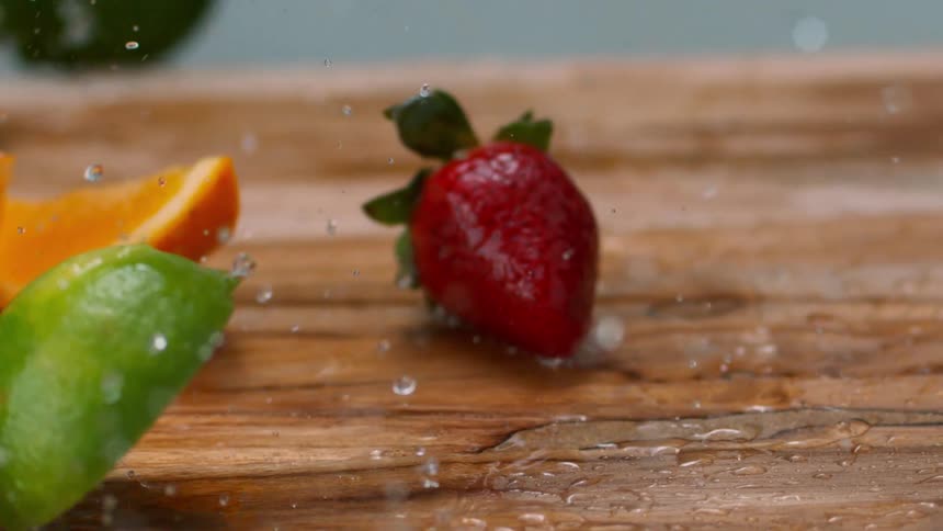 Freshly washed lime orange and strawberries falling to a cutting board