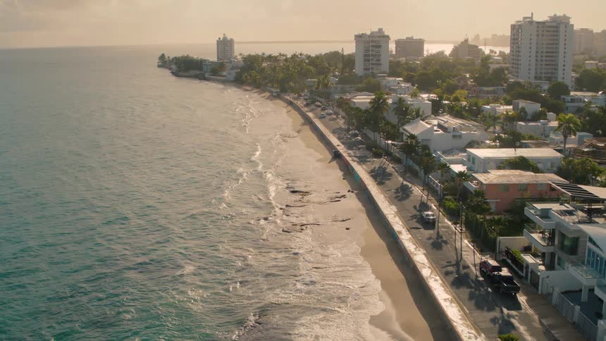 Waves crash onto the shore of a beach just below a city neighborhood