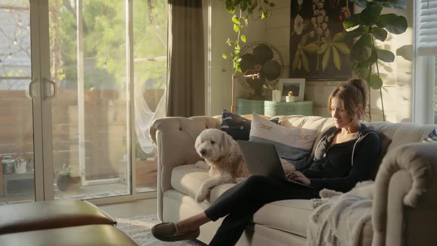 A woman sits on the couch with her dog