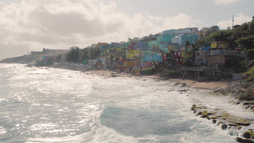 A graveyard filled with many burial plots is located along the shore of the ocean nearby a large residential area