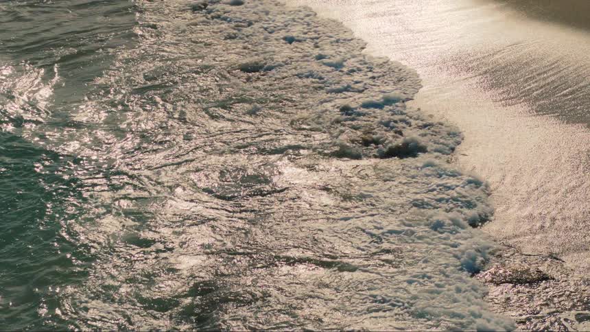Sea waves crash against the shore at sunset