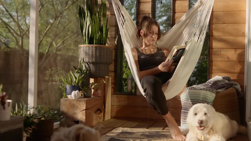 A woman is laying in a hammock reading a book