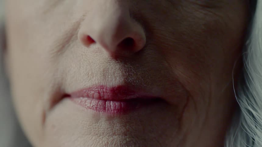 An elderly woman sits with her lips pursed