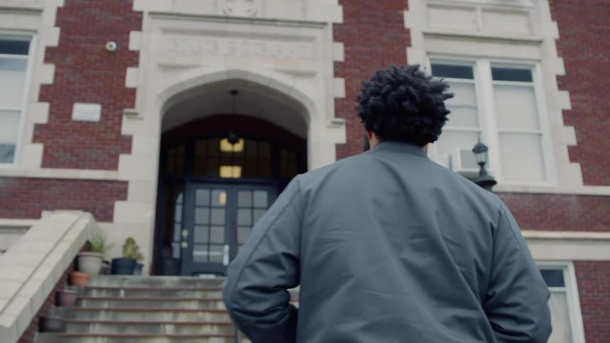 A man walks up concrete steps towards a large brick building