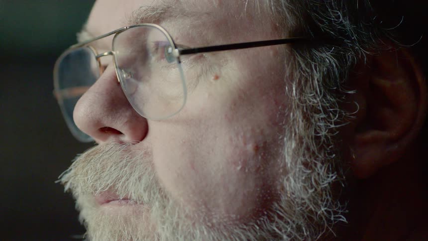 An older white man with a beard and glasses stares into the distance