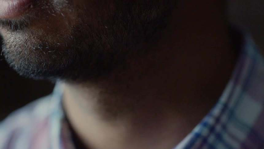 An indian man wearing a plaid shirt turns his head and stares