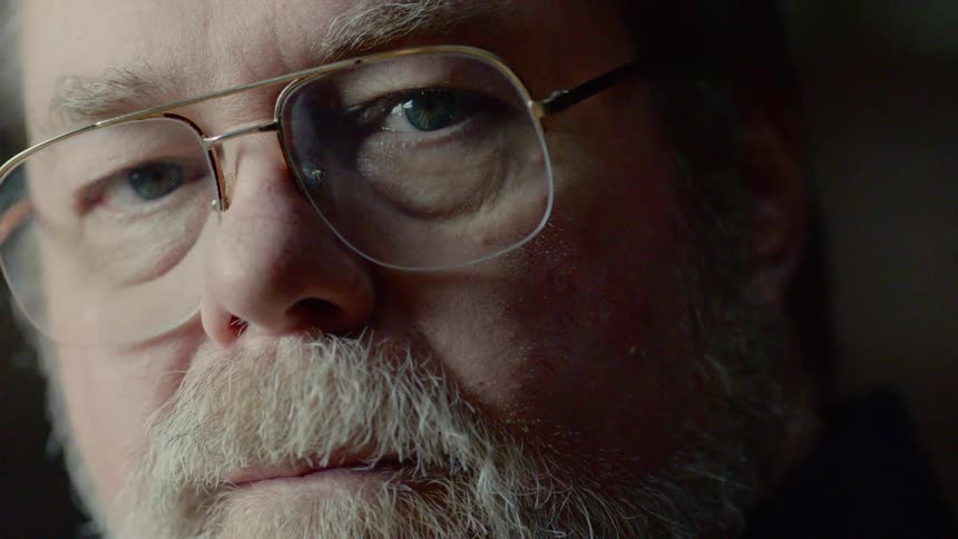 An older white man with a beard and glasses stares