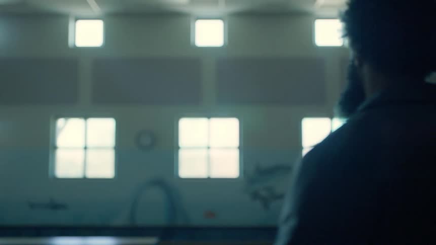An african american male enters a school cafeteria filled with empty tables where pictures of marine life adorn the walls
