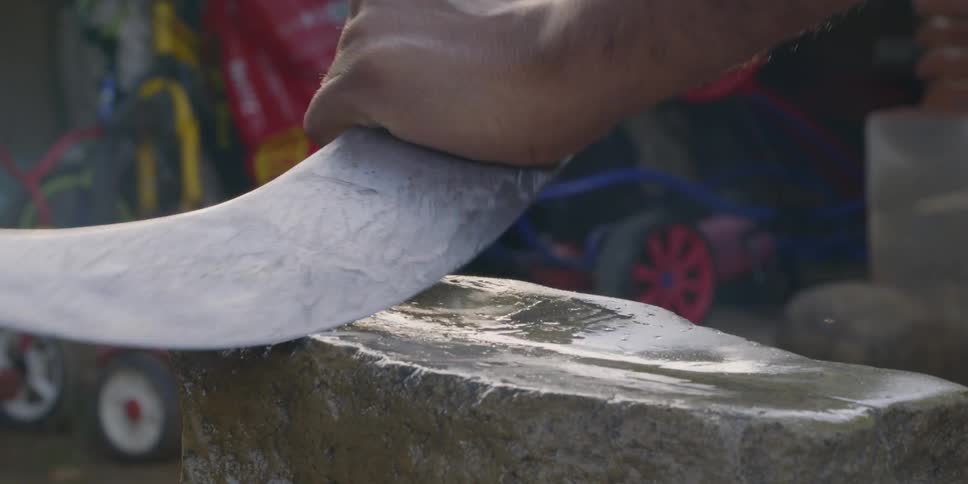 A person sharpens a large knife on a huge whetstone