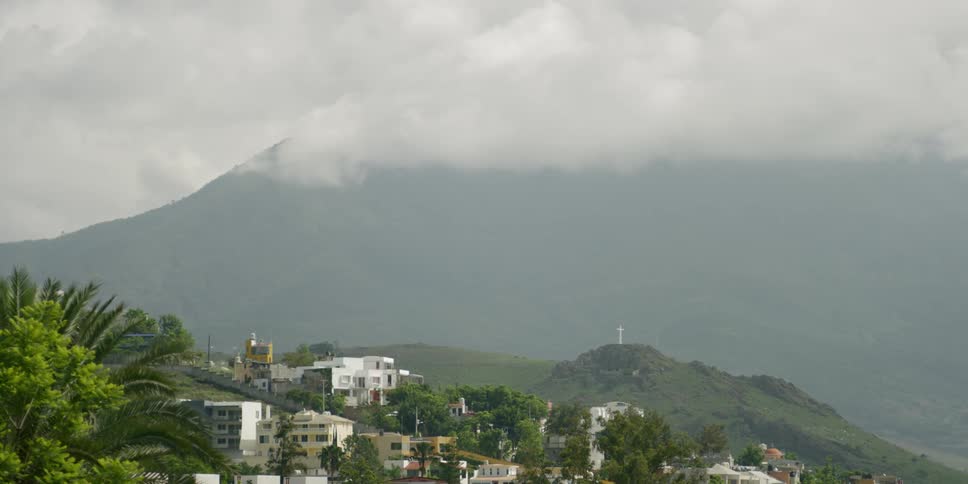 A cluster of buildings is located on a hillside near a towering mountain range