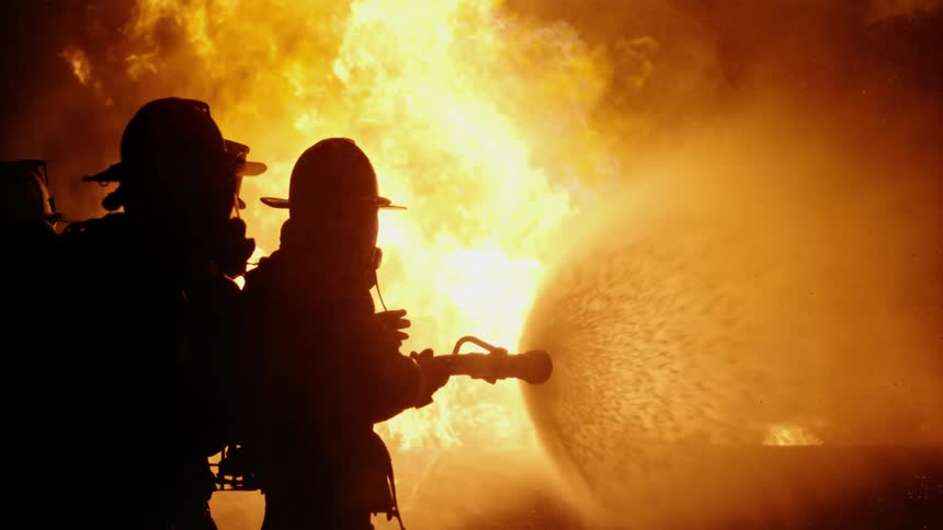 Firefighters point a hose at large flames