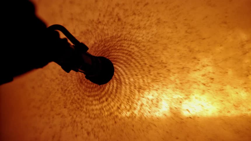 Water casts off in a spiral from a fire hose with flames in the background