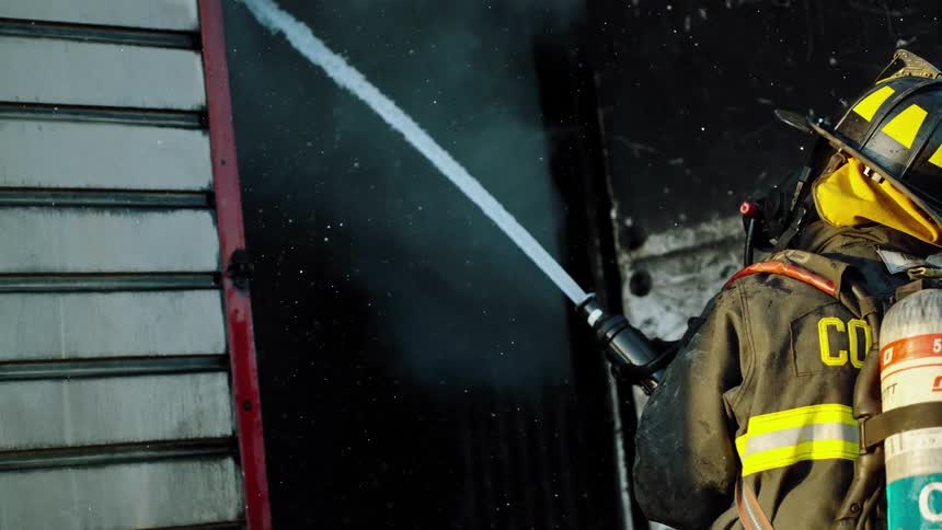A firefighter sprays water into a burned building