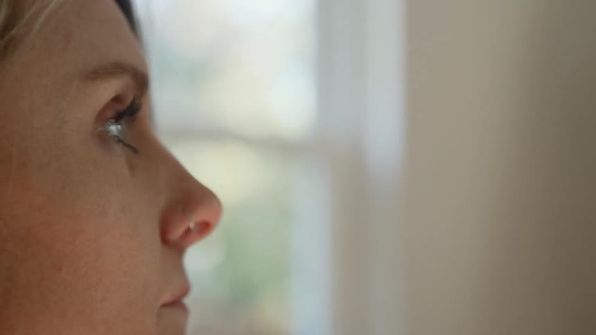 A woman with blonde hair and a nose piercing looks downward before gazing forward