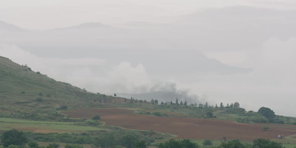 A large cleared expanse of brown soil at the base of a green hill slope