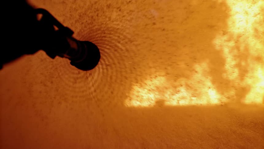 Fire hose spraying a roaring fire